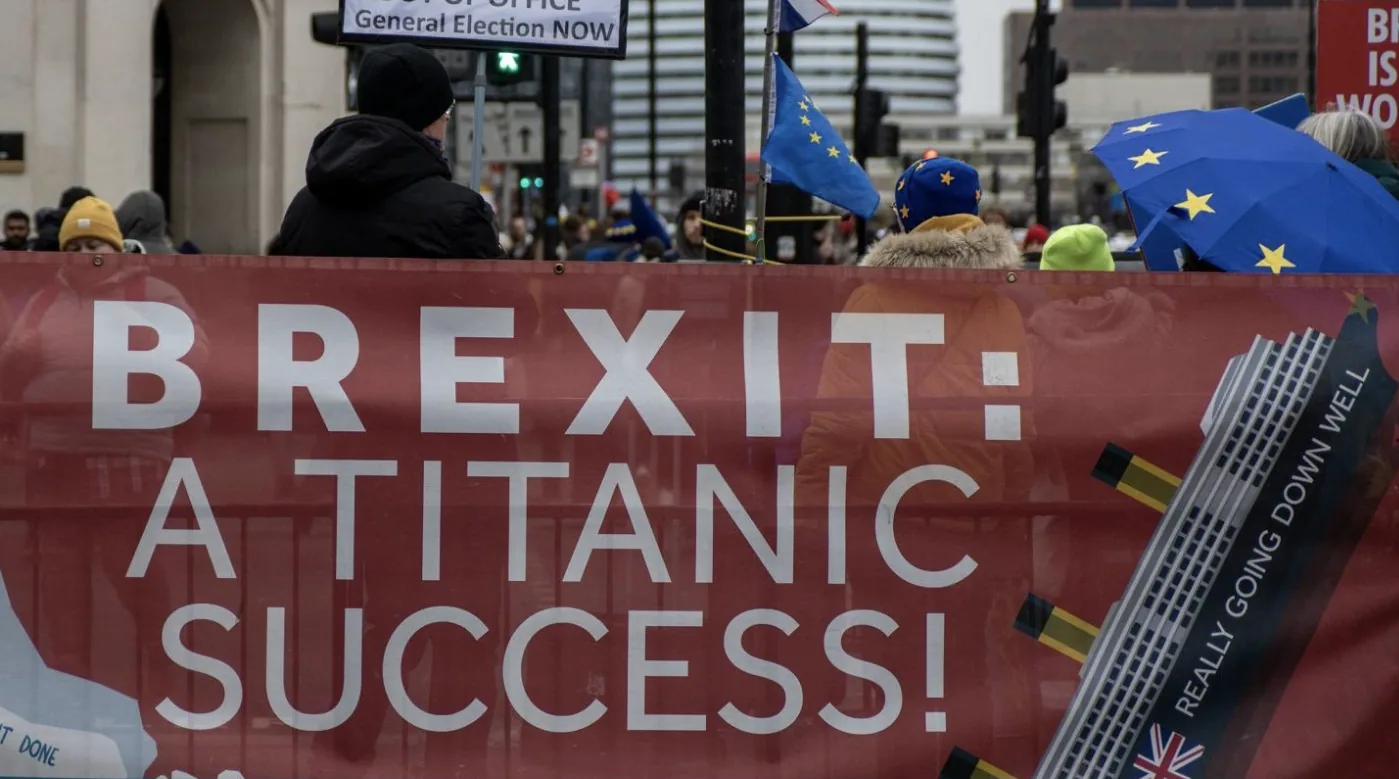 Striscione durante una manifestazione contro la Brexit con la scritta ironica "Brexit: a Titanic success!" e bandiere europee sullo sfondo.
