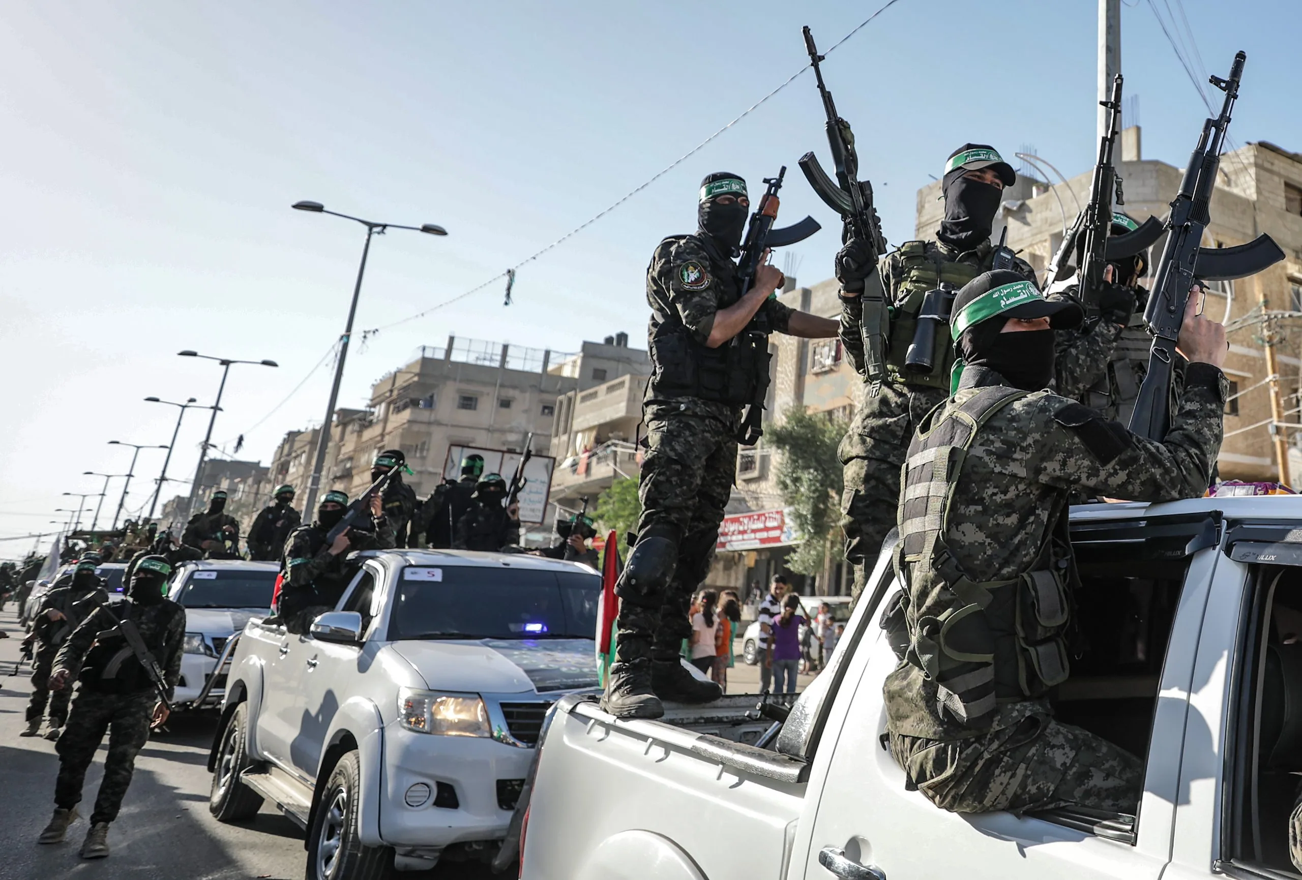 Miliziani di Hamas in parata armata su veicoli scoperti a Gaza, tra la folla e le bandiere.