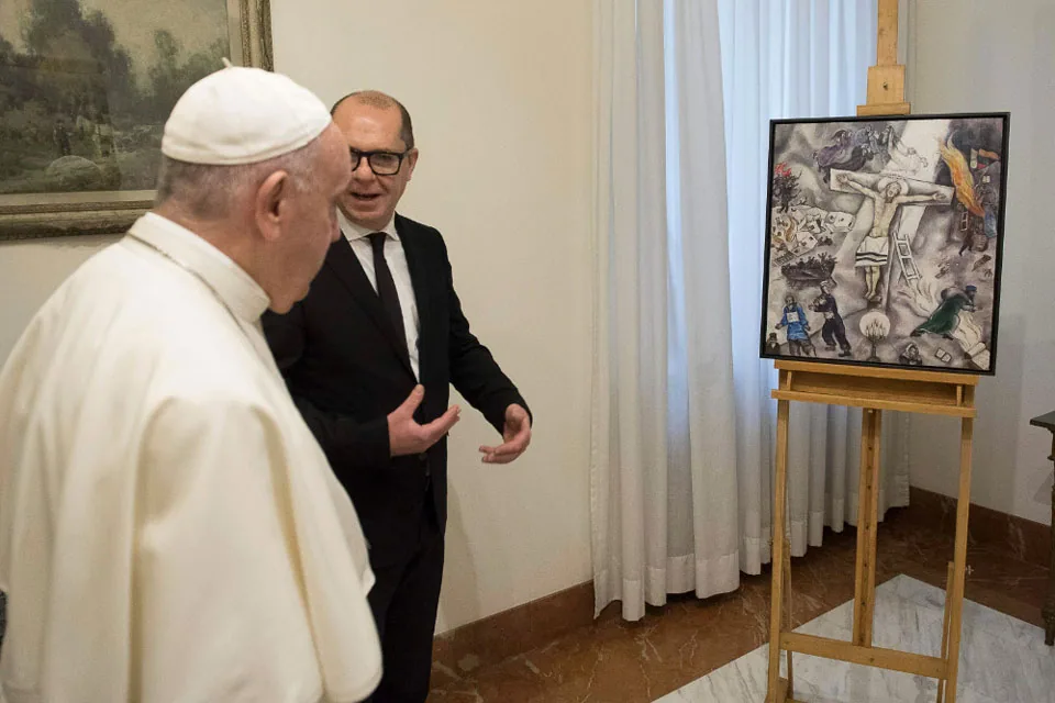 Papa Francesco osserva la "Crocifissione bianca" di Chagall durante un'esposizione, accompagnato da un curatore o storico dell’arte.