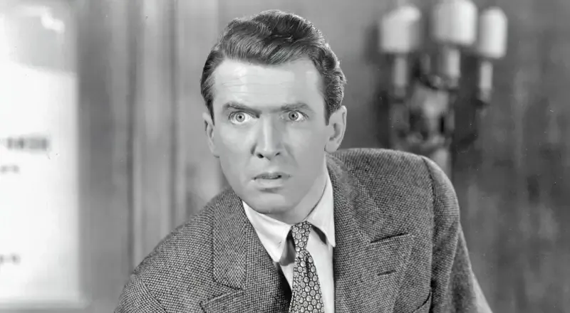 Scena in bianco e nero da un film d’epoca: uomo in abito elegante con sguardo teso, in primo piano.