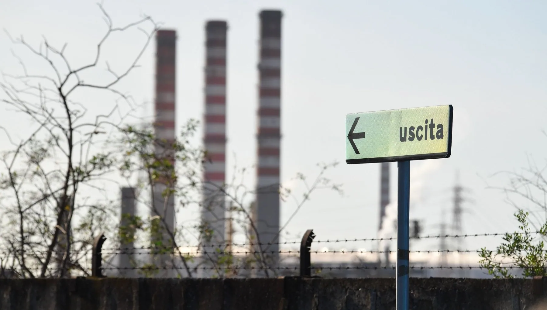 Ciminiere industriali e cartello "uscita", simbolo del declino manifatturiero italiano