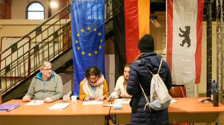 Una cittadina al seggio elettorale a Berlino durante le elezioni politiche 2024 in Germania, con bandiere dell’UE e del Land di Berlino sullo sfondo.