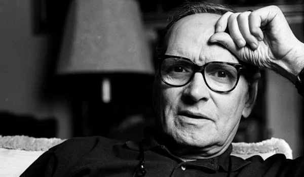 Ritratto in bianco e nero di Ennio Morricone, seduto con espressione riflessiva, simbolo del suo genio musicale