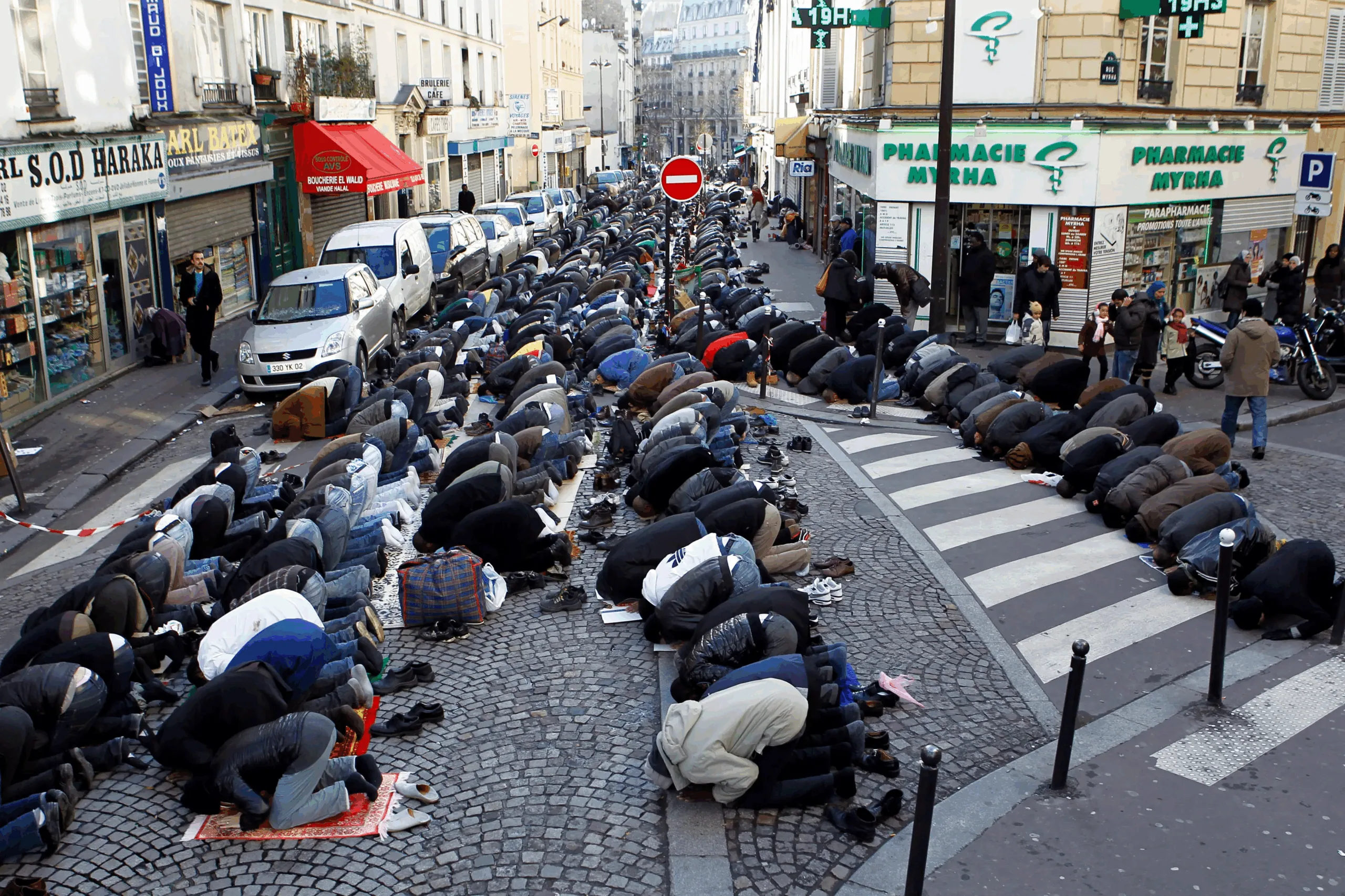 Fedeli musulmani pregano in strada durante la preghiera collettiva del venerdì in un quartiere urbano europeo.