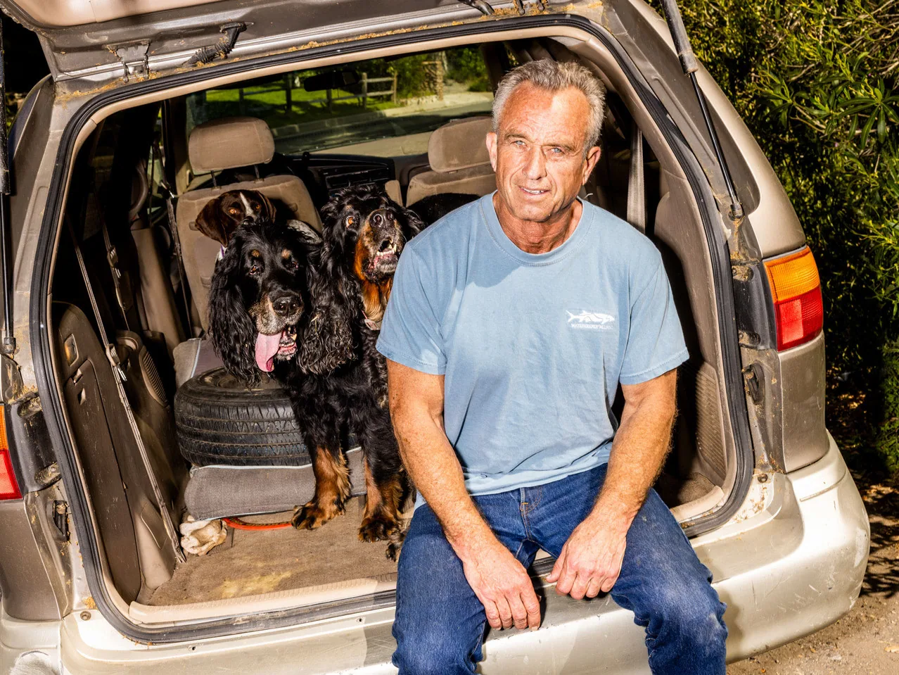 Robert Kennedy Jr. seduto sul retro di un’auto con due cani, in un contesto informale all’aperto