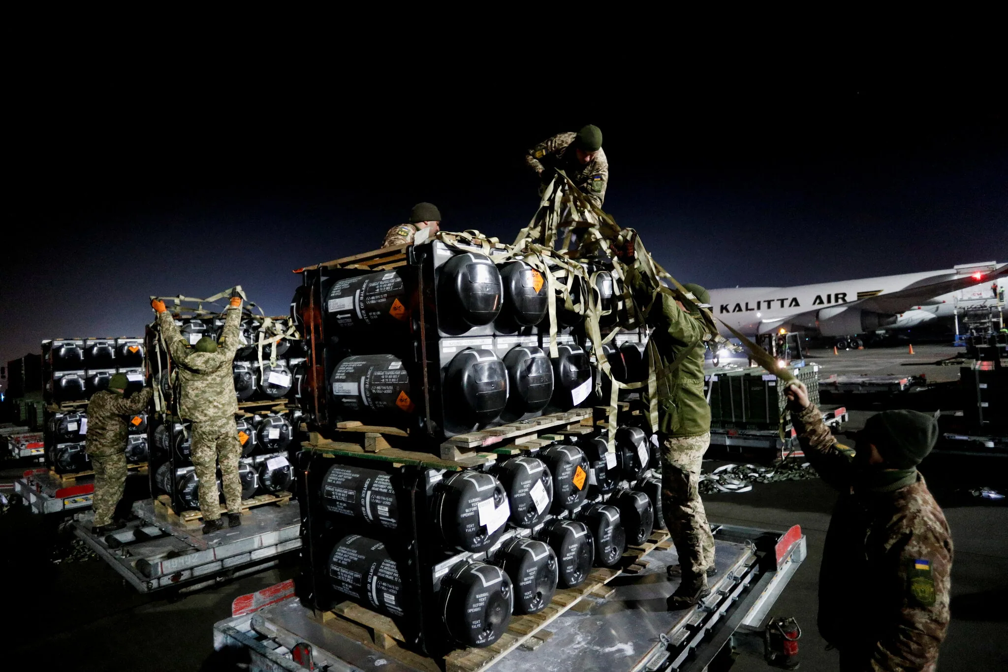 Soldati NATO caricano equipaggiamento militare in un aeroporto europeo per missione di supporto all’Ucraina contro l’invasione russa.
