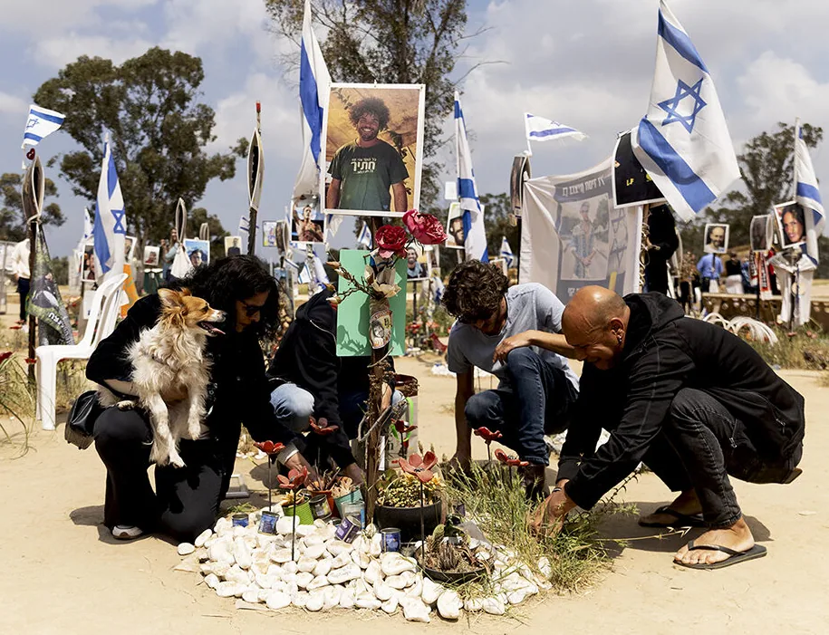 Persone inginocchiate depongono fiori su una tomba decorata con bandiere israeliane e la foto di un giovane, durante una commemorazione in Israele.