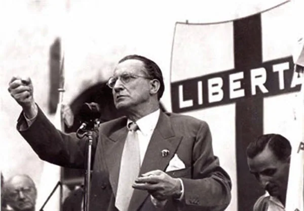 Alcide De Gasperi tiene un discorso pubblico davanti a un manifesto con la scritta "Libertà".