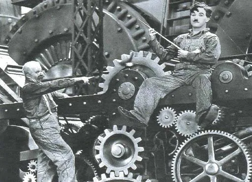 Charlie Chaplin tra gli ingranaggi di una macchina industriale nel film "Tempi moderni", simbolo della critica alla società industriale e tecnocratica.